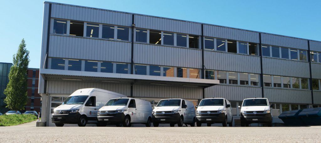 Moderne Firmenzentrale der NOVISOL AG mit mehreren Lieferwagen vor einem Bürogebäude mit Metallfassade.